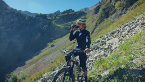 un ciclista de montaña bebe de su botella de agua rodeado de altas montañas