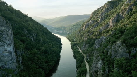 scenic view of the danube river, flanked by lush green mountains with the iconic rock sculpture of decebalus in dubova, romania