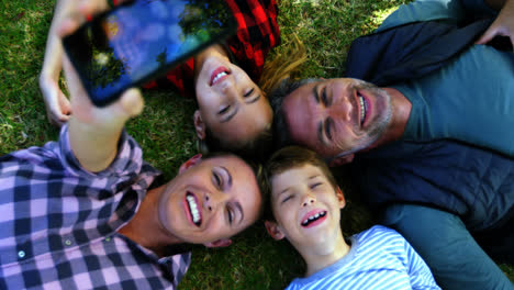 familia feliz acostada en el césped y tomando una selfie