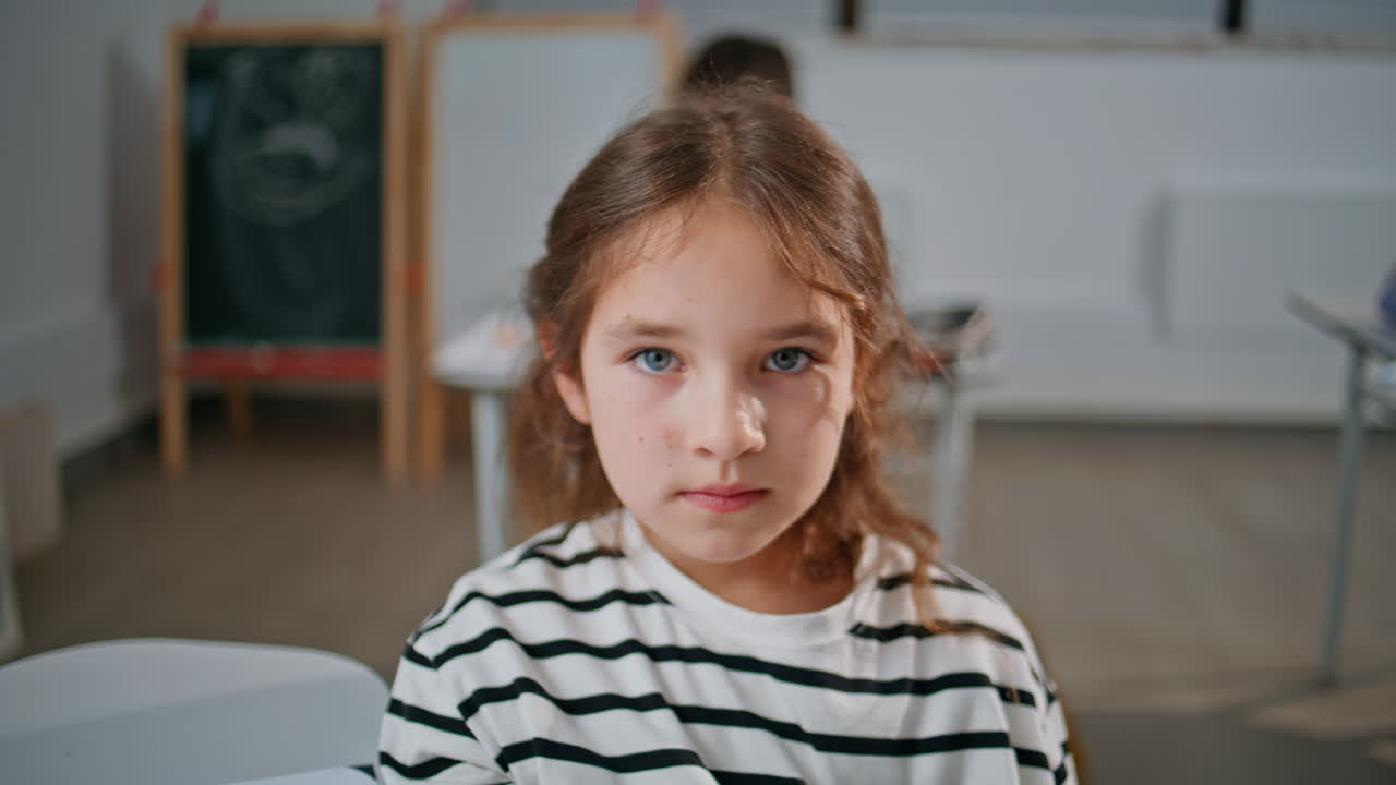 Portrait serious girl posing camera sitting in classroom. Smart pupil schooling