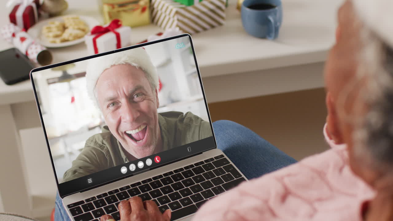 mujer afroamericana con sombrero de santa teniendo llamada de video portátil con hombre caucásico feliz
