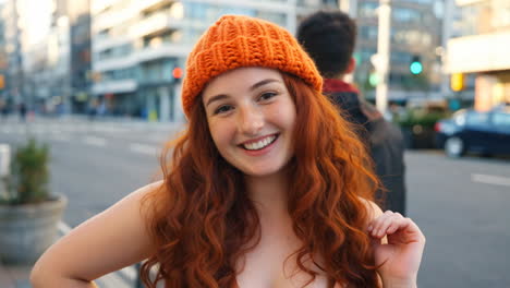 smiling redhead woman with orange beanie in city