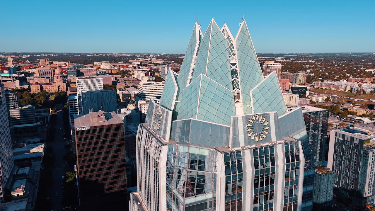 Austin, USA, 21 novembre 2025: Primo piano della corona architettonica della Frost Bank Tower ad Austin. Scatto dettagliato di un grattacielo di vetro con un design unico del tetto a punta e il Campidoglio dello Stato del Texas in lontananza.