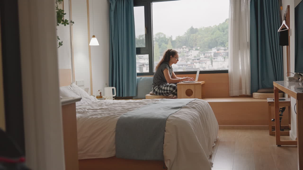 Lys morgen belyser en uoppredd seng. Stille refleksjon idet byens silhuett kommer til syne. Koselig interiør fanger et rolig øyeblikk av gjesten som observerer bylandskapet gjennom vinduet