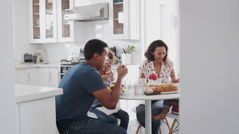 Young-family-sitting-at-table-in-the-kitchen-eating-together,-selective-focus,-panning-shot