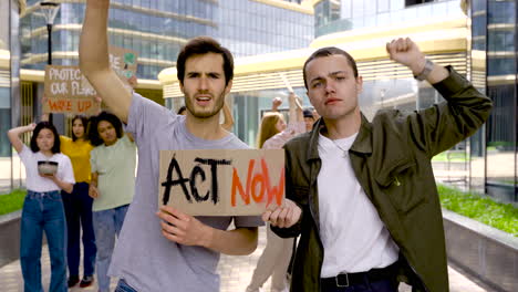 young men holding act now board on a protest while raise their fists and walk towards the camera