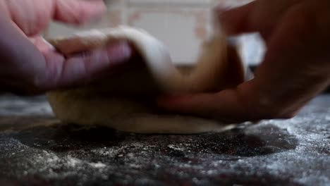 working on a home made pizza dough with the bare hands on a marble kitchen counter. natural window light