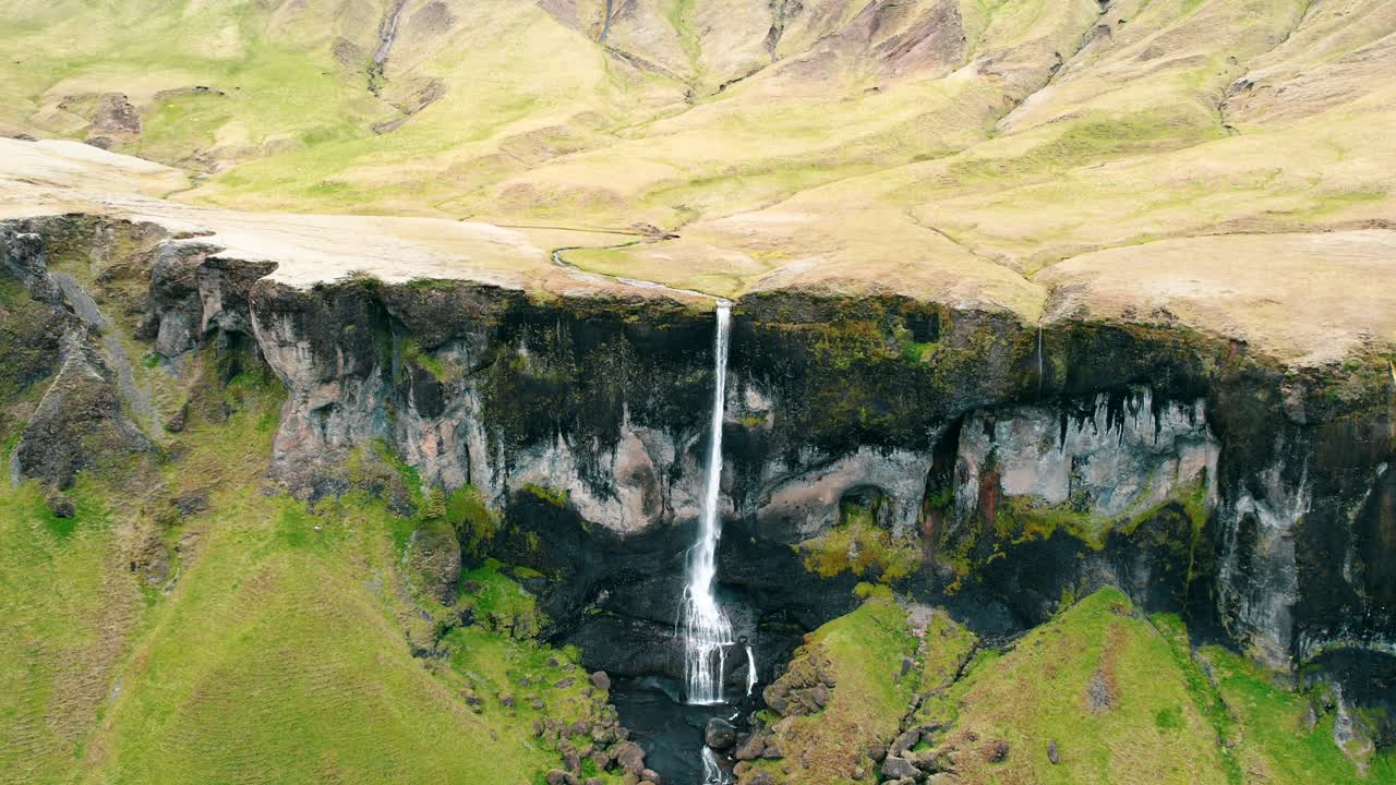 una cascada larga y delgada en una escarpa rocosa alta en las montañas, islandia