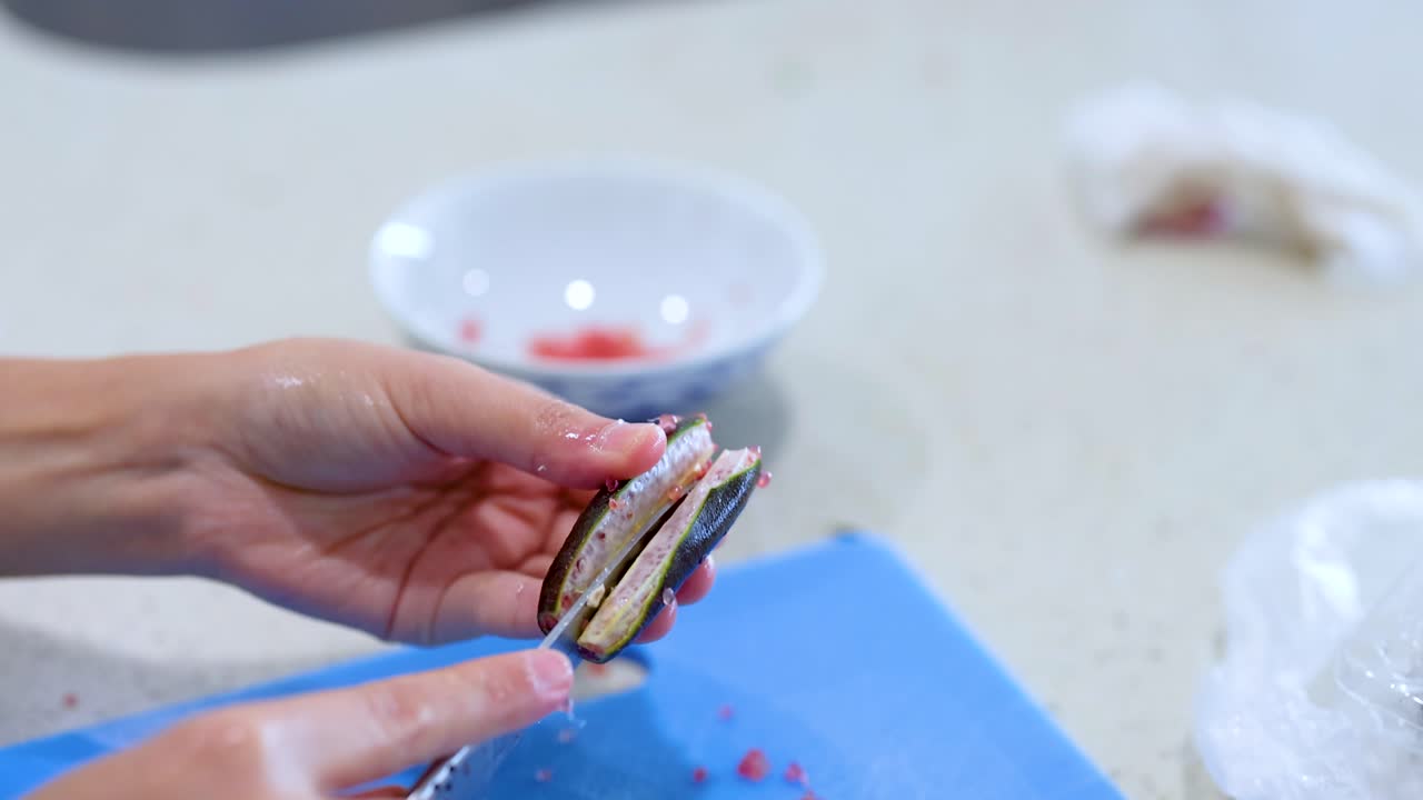 Hands skillfully slice fish on a blue cutting board. Bright kitchen lighting enhances the clean, culinary setting