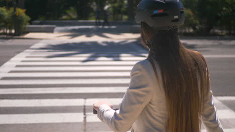 Vista-Trasera-De-Una-Mujer-Irreconocible-Con-Scooter-Eléctrico-Esperando-En-El-Cruce-De-Peatones-A-Que-Se-Mueva-La-Luz-Verde