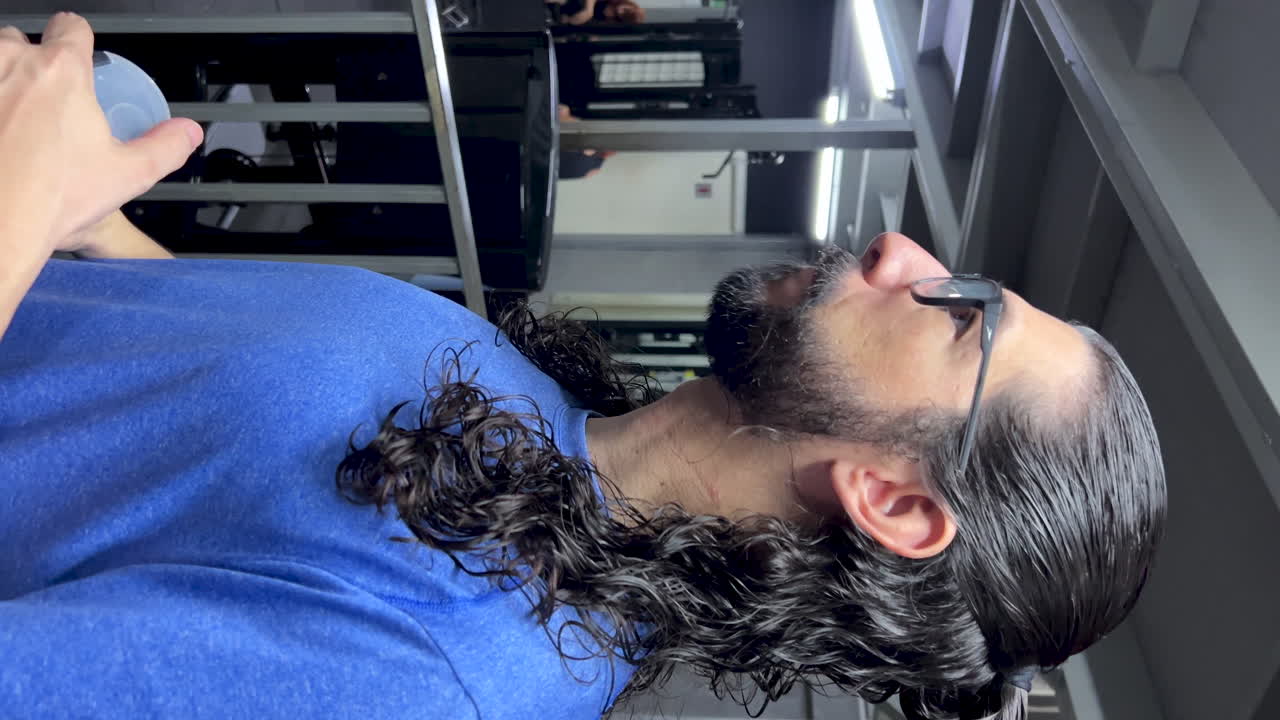 hombre latino con barba y cabello largo hidratando en el gimnasio