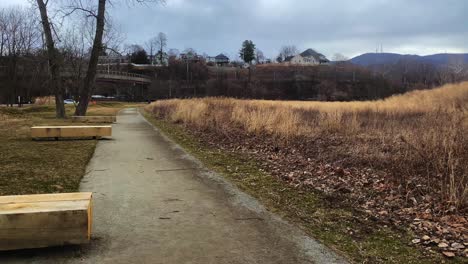 a walking path with benches in a public green space next to a small city