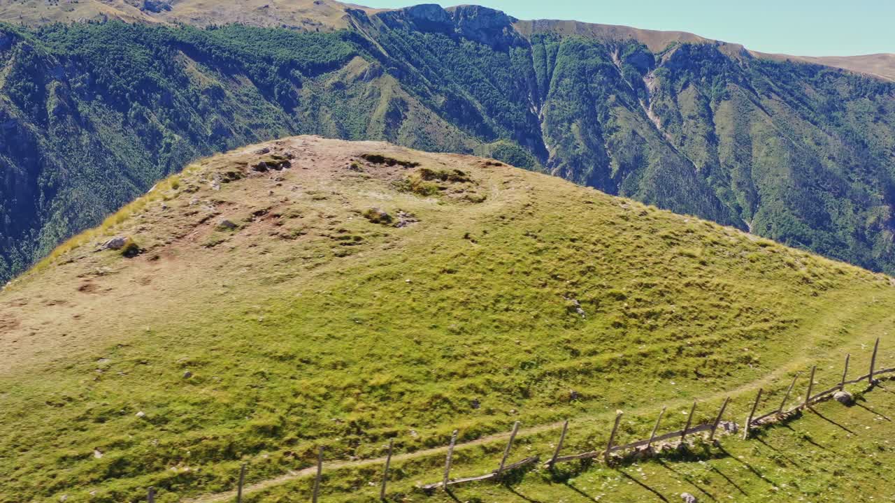 Majestic light green highlands by dark green deep crevasses in background mountains, aerial
