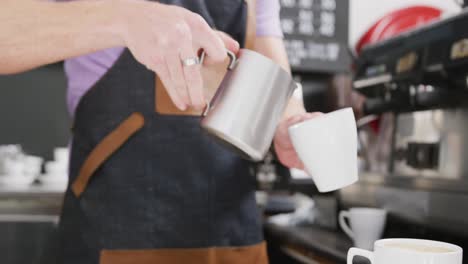 barista masculino caucásico con delantal añadiendo leche al café en una cafetería