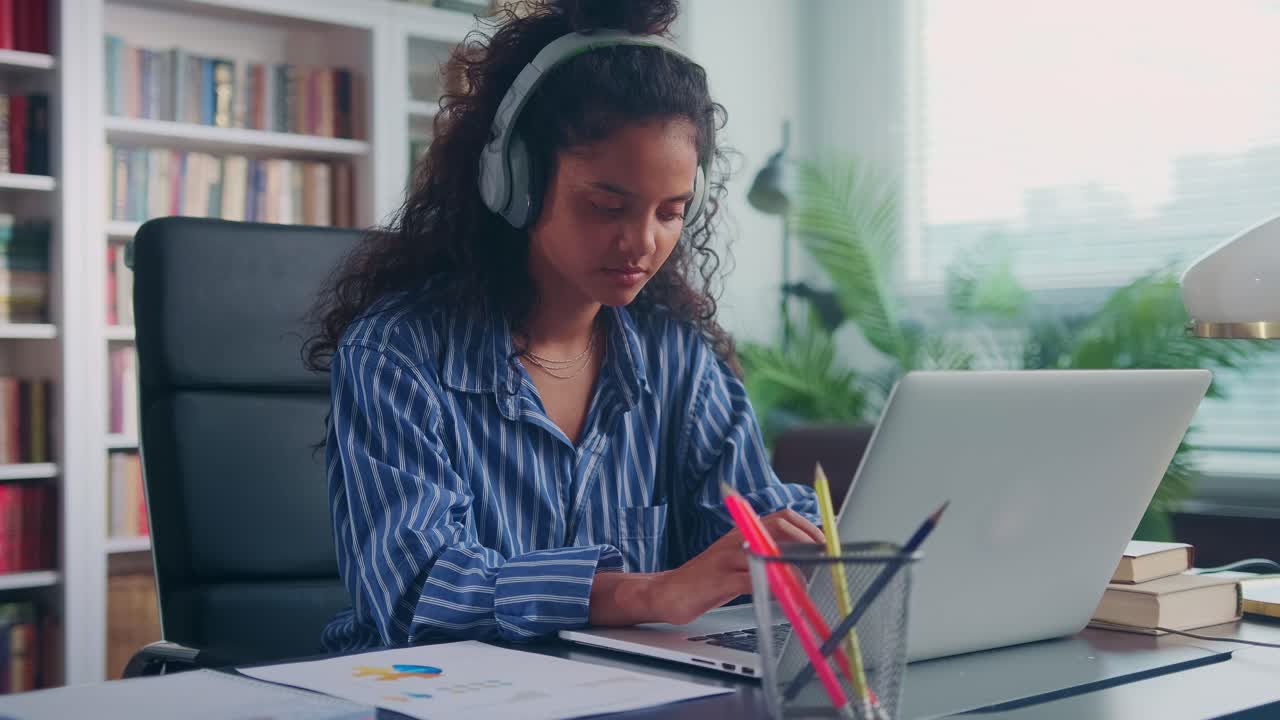 Young indian woman listening to music on headphones and working with laptop