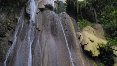 A-stunning-War-Inkabom-Waterfall-on-Batanta-Island-in-Raja-Ampat,-Indonesia,-cascades-down-a-rocky-cliff-into-a-serene-pool-below,-surrounded-by-lush-greenery