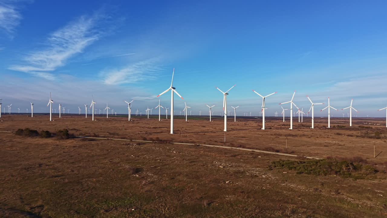 As turbinas eólicas se elevam em um campo aberto sob um céu azul durante o dia, demonstrando os esforços de energia renovável em uma área rural
