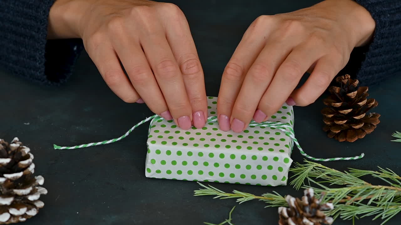 여자 손은 녹색과 흰색 포장으로 선물 상자의 밧줄을 묶습니다.