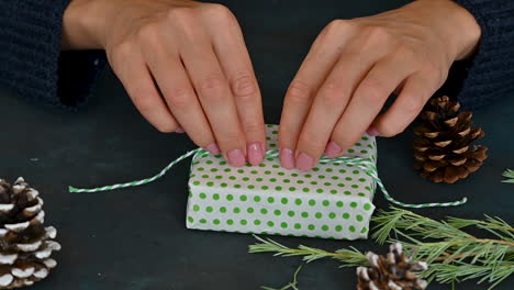 Manos-De-Mujer-Atan-La-Cuerda-De-Una-Caja-De-Regalo-Con-Envoltura-Verde-Y-Blanca