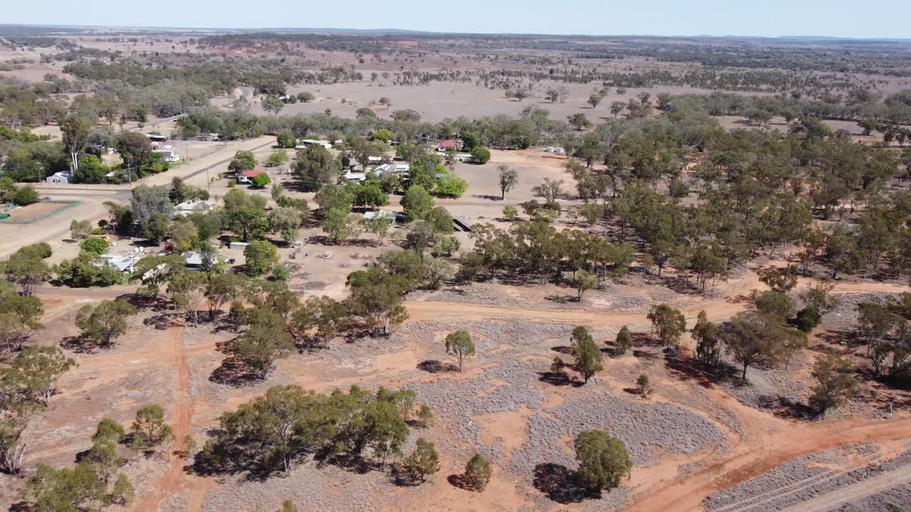 drone volando sobre tierra boscosa hacia un pueblo muy pequeño en el interior de australia