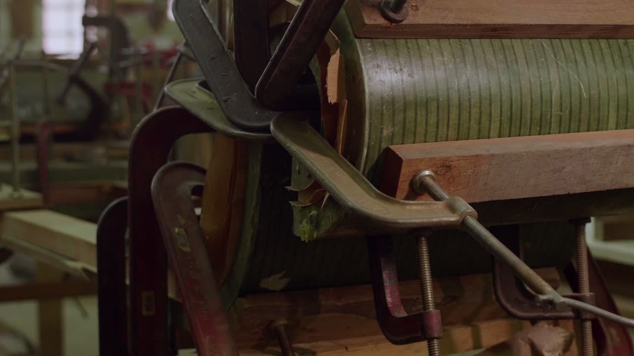 A close-up of woodworking clamps securing curved wooden parts in place, with green strips and wooden frames held tightly together, likely in a furniture-making or restoration process.