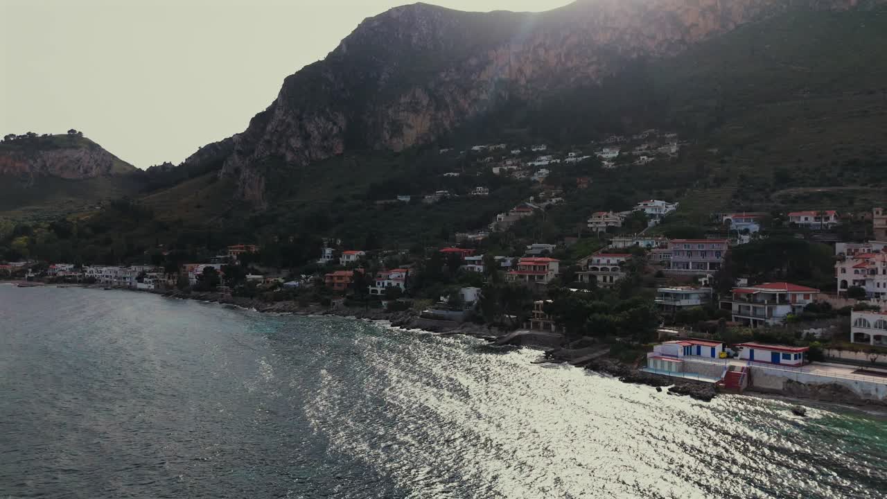 Low angle slow motion drone shot over seaside houses on the Tyrrhenian coast near Capo Zafferano and Sant Elia with mountain backdrop in Sicily Italy