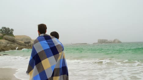 rear view of caucasian couple in blanket walking on the beach 4k