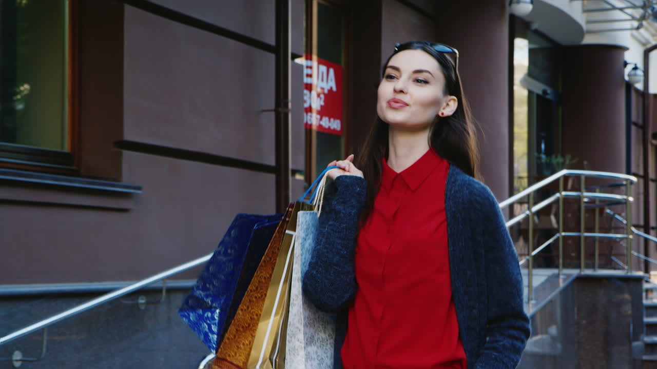 세련된 여성 모델의 외모는 쇼핑백을 들고 도시를 통과합니다.