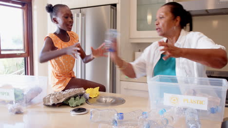 grandmother and granddaughter sorting plastic bottles for recycling in kitchen, at home