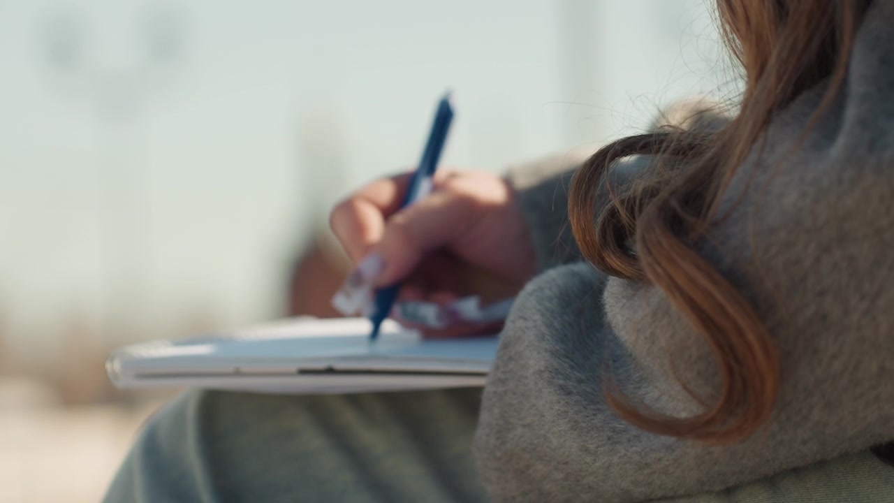 Sketching on bench with flowing curls. Relaxed atmosphere captured in city scene artwork sketching. Creative drawing session on park bench with soft sunlight and blurred city background