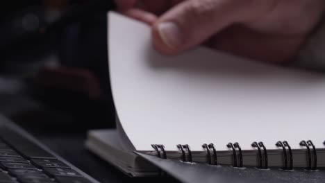 close up of man's hands writing in spiral notepad placed on wooden black desktop