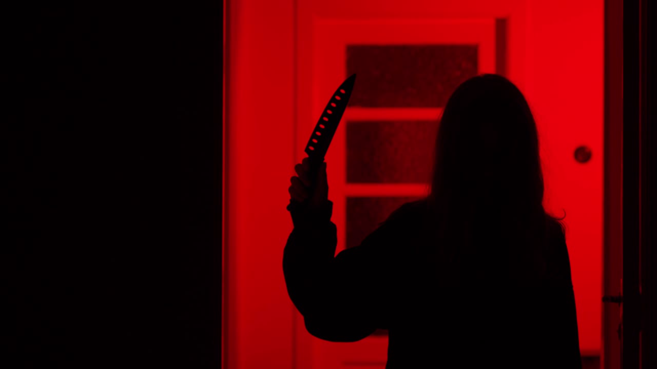 Scary girl walking up to camera with a kitchen knife on a red light background.