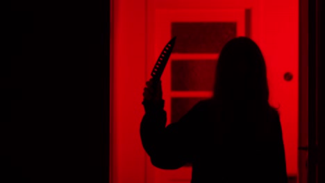 scary girl walking up to camera with a kitchen knife on a red light background.