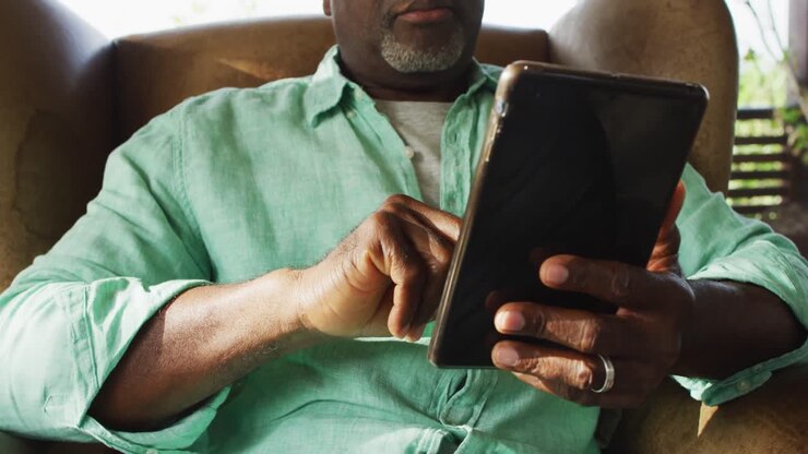 African american senior man in living room sitting in armchair using tablet