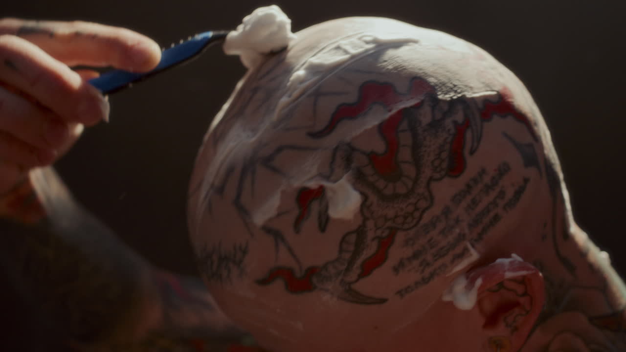 Close Up of Man Shaving Tattooed Scalp Covered in Foam with Razor