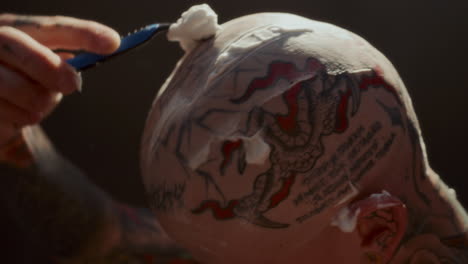 close up of man shaving tattooed scalp covered in foam with razor