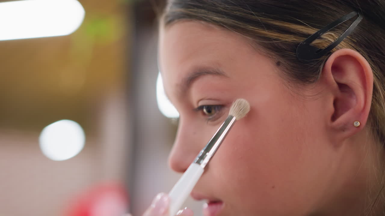 vista de primer plano de una mujer aplicando polvo de maquillaje en el ojo usando un pincel de maquillajes, centrarse en la aplicación precisa del maquillaje, haciendo hincapié en la técnica y las herramientas de maquillaja