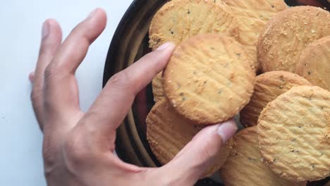 hand holding a round cookie from a pile on a plate