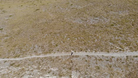 Toma-Aérea-De-Un-Hombre-Caminando,-Caminando-Solo-En-La-Montaña-Griega-Kissavos-En-La-Región-De-Tesalia,-Vista-De-Drones,-Ruta-En-La-Montaña,-Estilo-De-Vida-Deportivo,-Manera-Saludable-De-Dejar-El-Paisaje-Marrón-Caminando