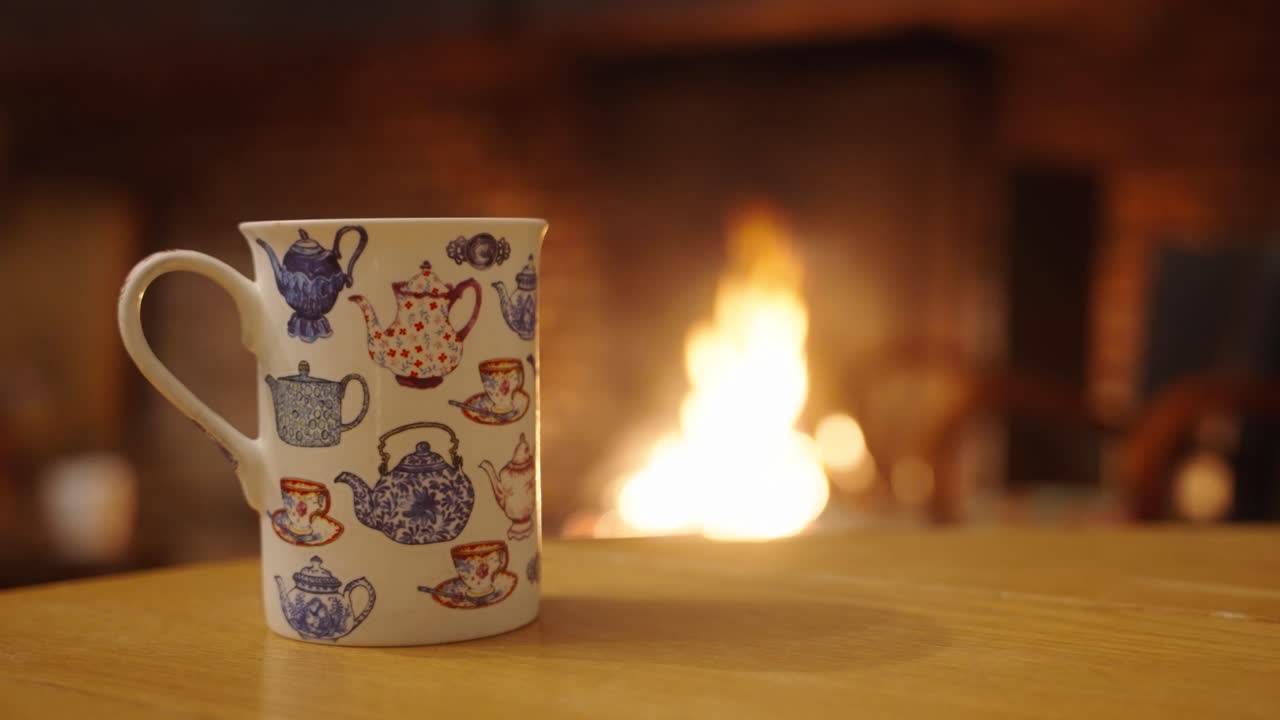 una taza de café con leche sentada junto a un fuego cálido en una mesa de madera dentro de una casa en una fría noche de invierno