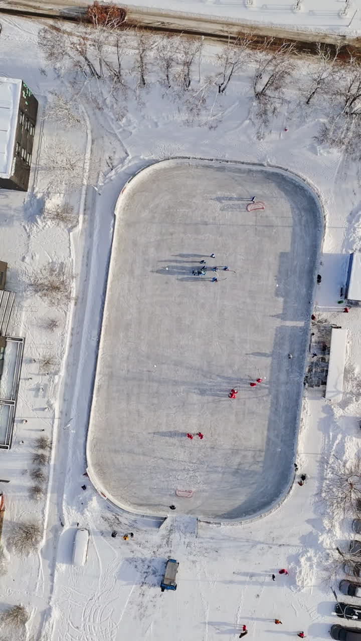 Screwdriver aerial view rising above ice hockey rink, on a sunny, winter day