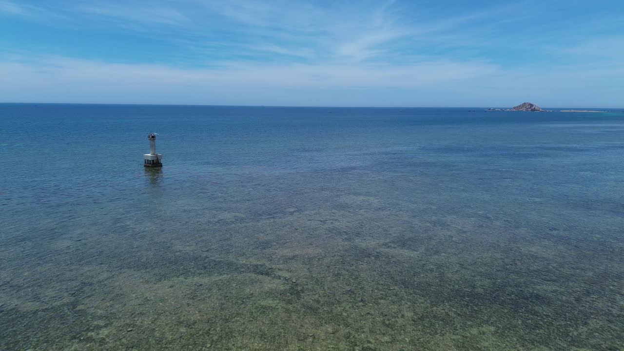 Drone advancing forward above the tranquil shallow waters of My Hoa Lagoon, with a lighthouse and islet in the distance under a clear sky. My Hoa Vietnam, famous kitesurfing spot during low season.