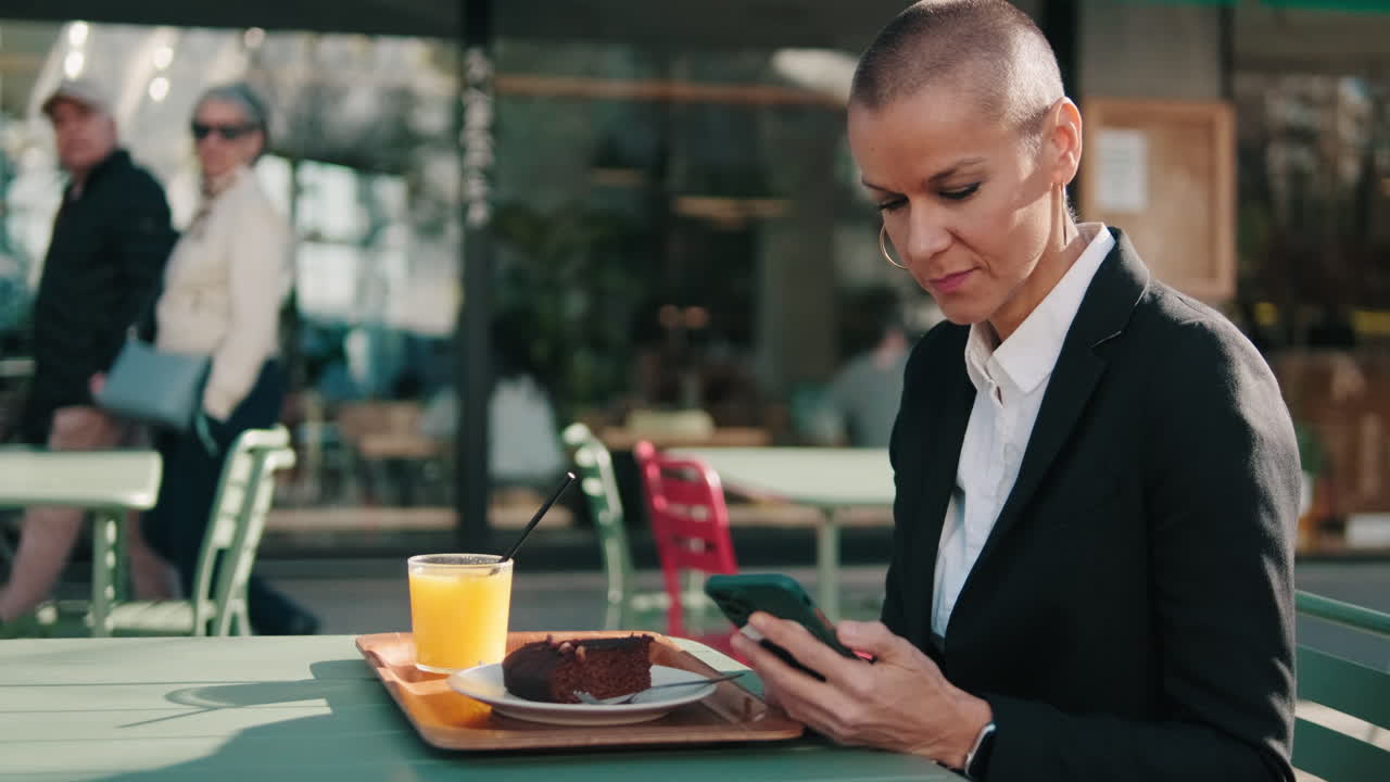 Woman with Shaved Head Using Smartphone at Outdoor Cafe