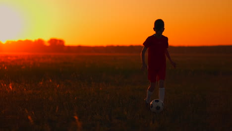 niño jugador de fútbol al atardecer corre con una pelota de fútbol en el campo de entrenamiento regateando desde el amanecer hasta el anochecer. camino al éxito. el concepto de lograr la meta de un atleta exitoso