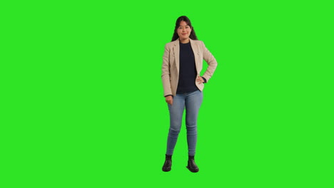 full length studio portrait of female teacher or businesswoman standing against green screen with hand on hip