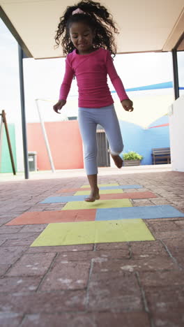 vertical video: in school playground, young african american girl is playing hopscotch