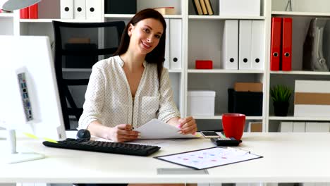 mujer de negocios sentada en la mesa leyendo y mirando a la cámara