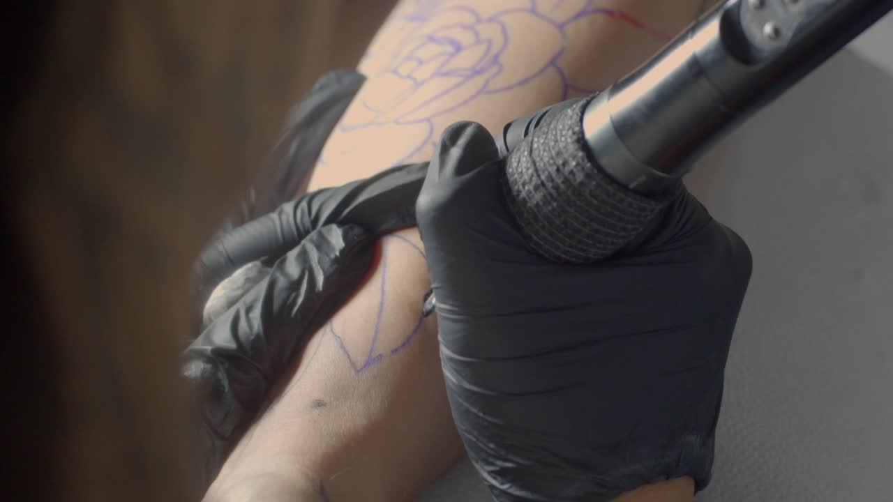 문신 아티스트는 검은 장갑을 사용하여 피부에 정밀하게 잎 디자인을 윤합니다. 직선으로 근접적으로 보십시오.