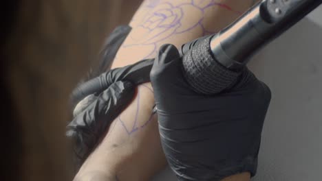el artista del tatuaje conforma un diseño de hoja con precisión en la piel usando guantes negros.