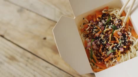 composition of box of pad thai with chopsticks on wooden background